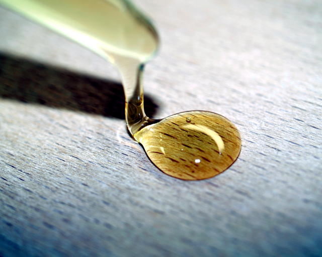 Honey-colored liquid drips from an applicator onto a beechwood surface.