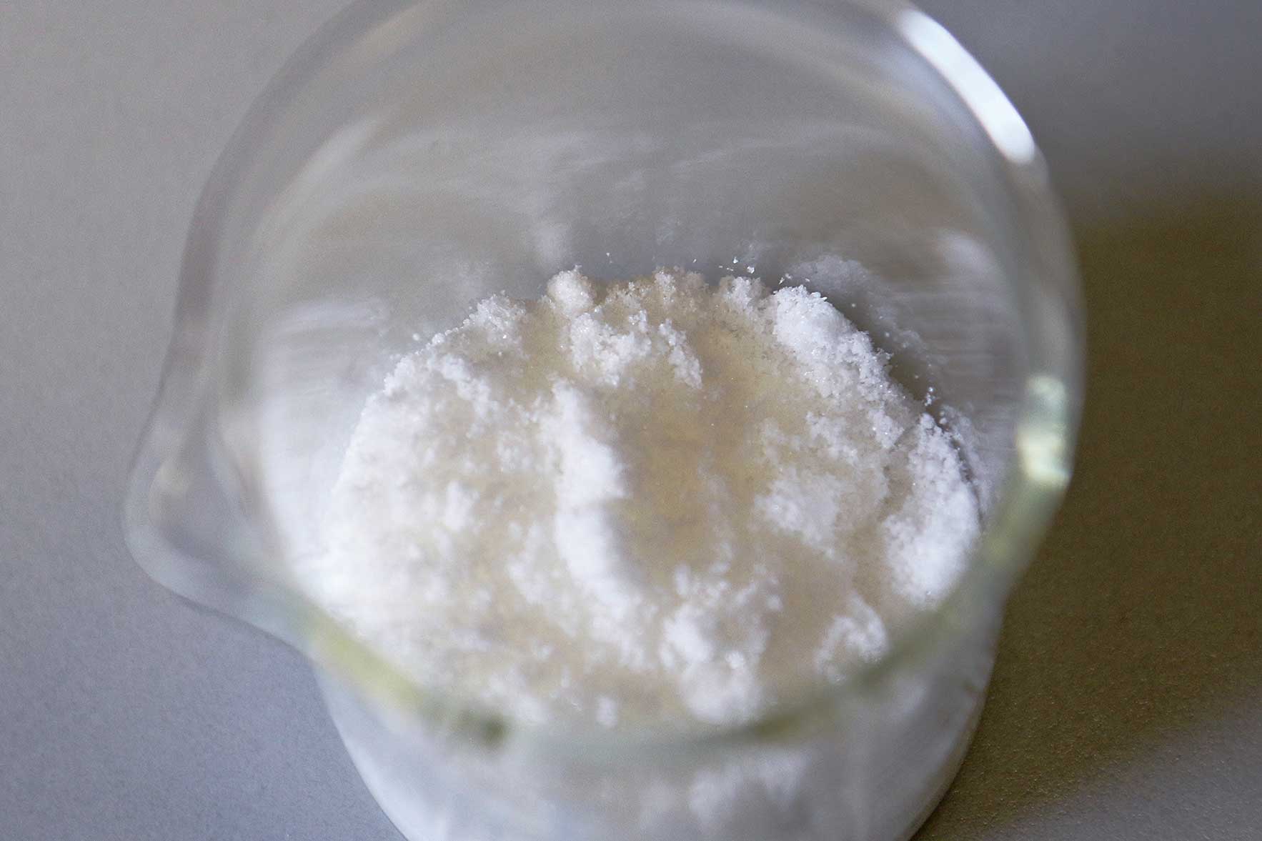 The photo shows a laboratory jar containing a white powder.