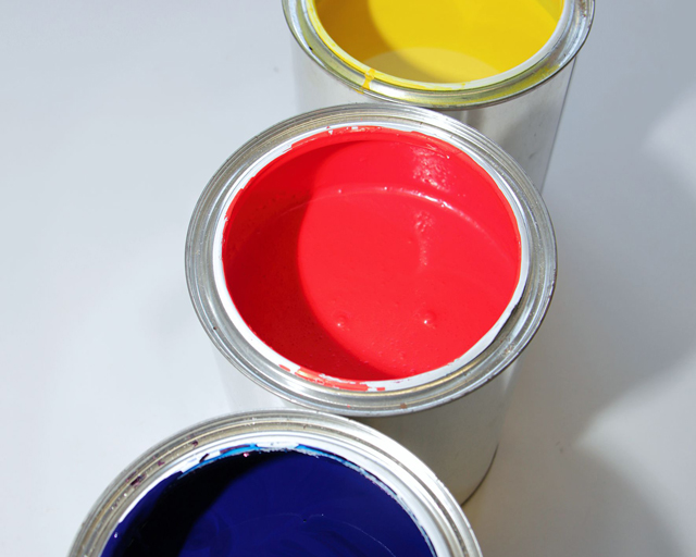 Drei Metalldosen mit flüssiger Farbe in Blau, Rot und Gelb.