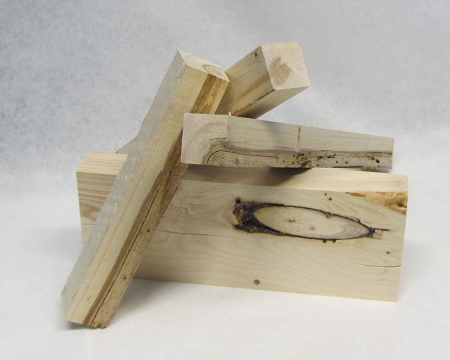 Das Foto zeigt vier aufeinander gestapelte Schnittholz-Stücke aus Fichte: drei Kantholz-Stücke mit einem Querschnitt von ca. 10 x 10 cm und ein Balkenstück mit einem Querschnitt von ca. 10 x 20 cm. 