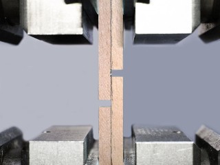 Das Foto zeigt eine Apparatur aus Metall, in die ein mehrteiliges, geklebtes Stück Buchenholz eingespannt ist und auseinandergezogen wird.