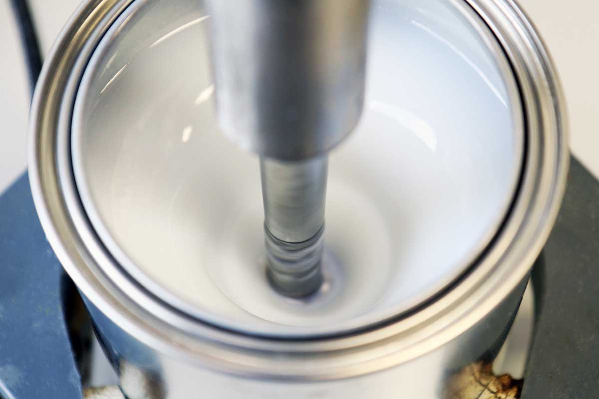 Das Foto zeigt eine Lackdose mit einer weißlich-transparenten Flüssigkeit, in die ein Rührstab eingetaucht ist.