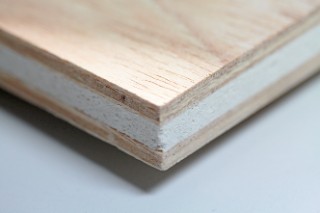 Das Foto zeigt den Querschnitt einer Platte. Die beiden Außenschichten bestehen jeweils aus einer ca. 5 mm dicken Schicht Sperrholz, der Blähglaskern ist hellgrau und ca. 8 mm dick.