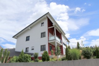 Das Foto zeigt ein Haus mit Garten. Die Fassade ist verputzt und zweifarbig gestrichen. 