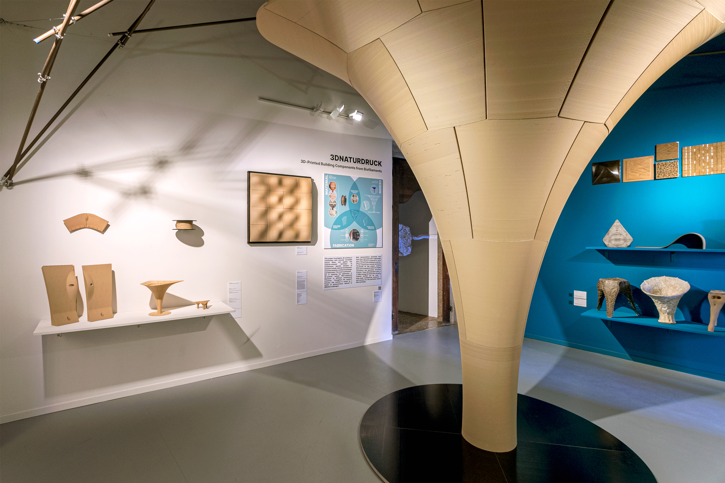 Das Foto zeigt einen Ausstellungsraum mit verschiedenen Exponaten. In der Mitte des Raumes steht eine raumhohe, trichterförmige Säule, die von unten nach oben immer breiter wird.