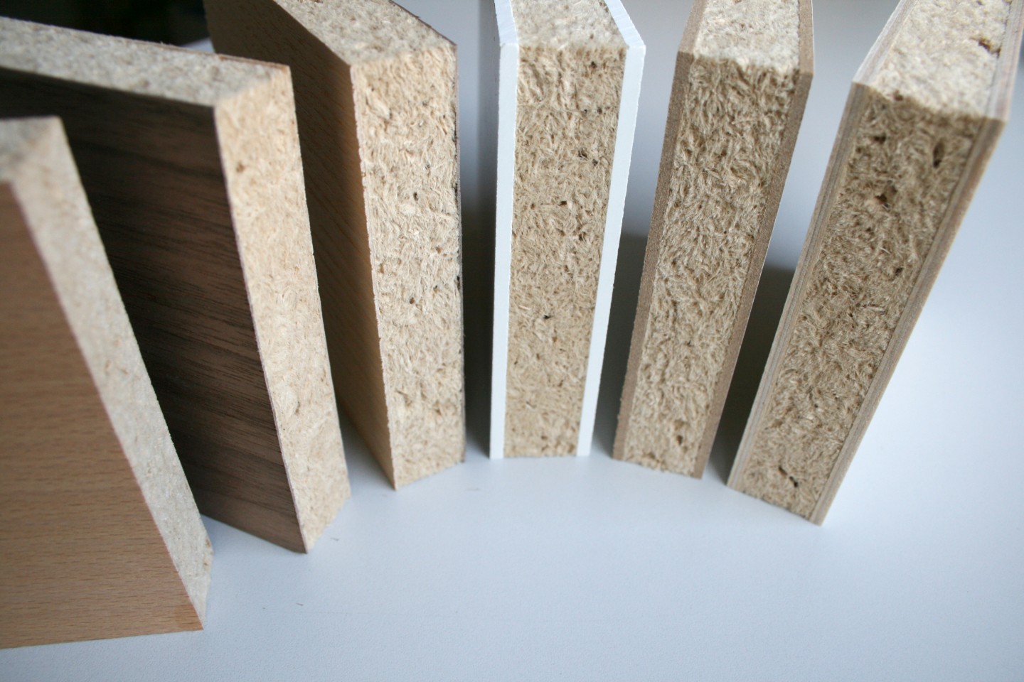 Auf dem Foto sind sechs Plattenstücke zu sehen. Sie haben alle einen Holzschau-Kern und beidseitig eine dünne Deckschicht. Die Deckschicht bestehen bei jedem Plattenstück aus einem anderen Material, zum Beispiel Buche-Furnier oder Holzfaserplatte. 