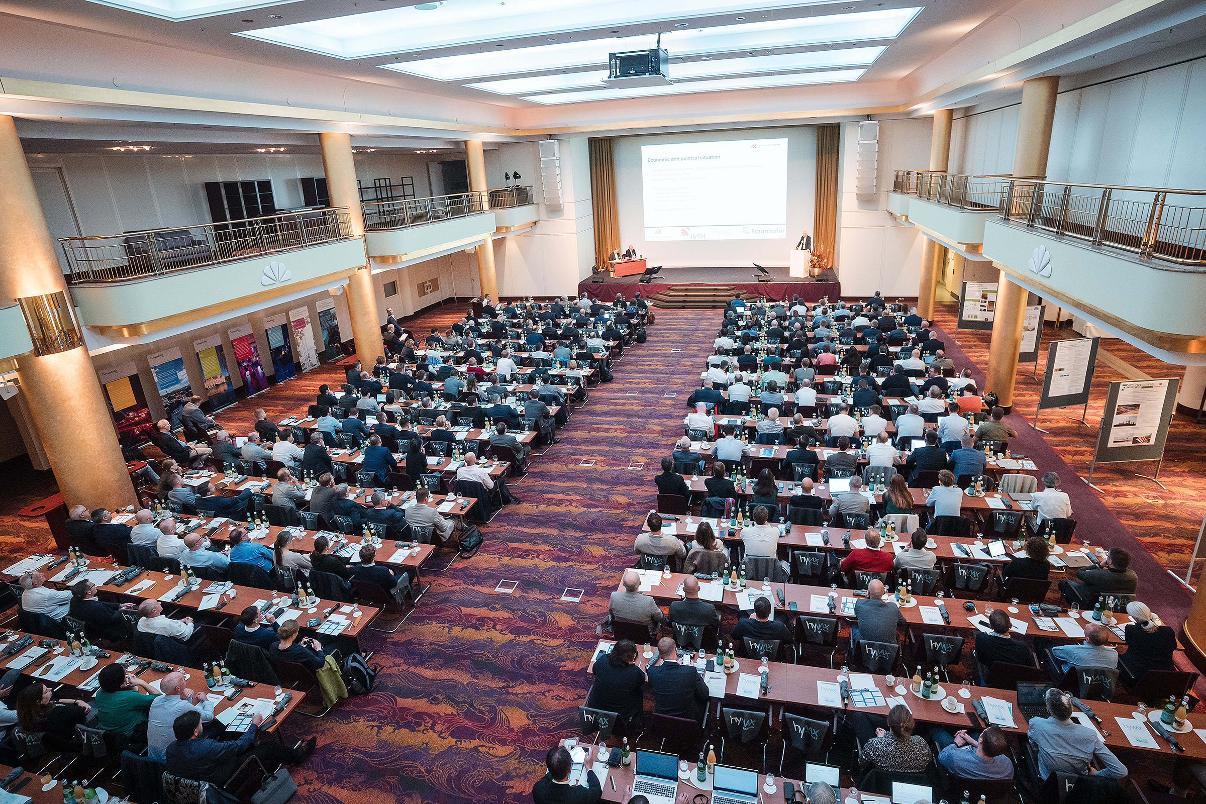 13. Europäischen Holzwerkstoff-Symposium in Hamburg Das Foto zeigt einen großen Raum mit Stuhlreihen, auf denen Menschen sitzen, und einem Podium, auf dem Redner sitzen.