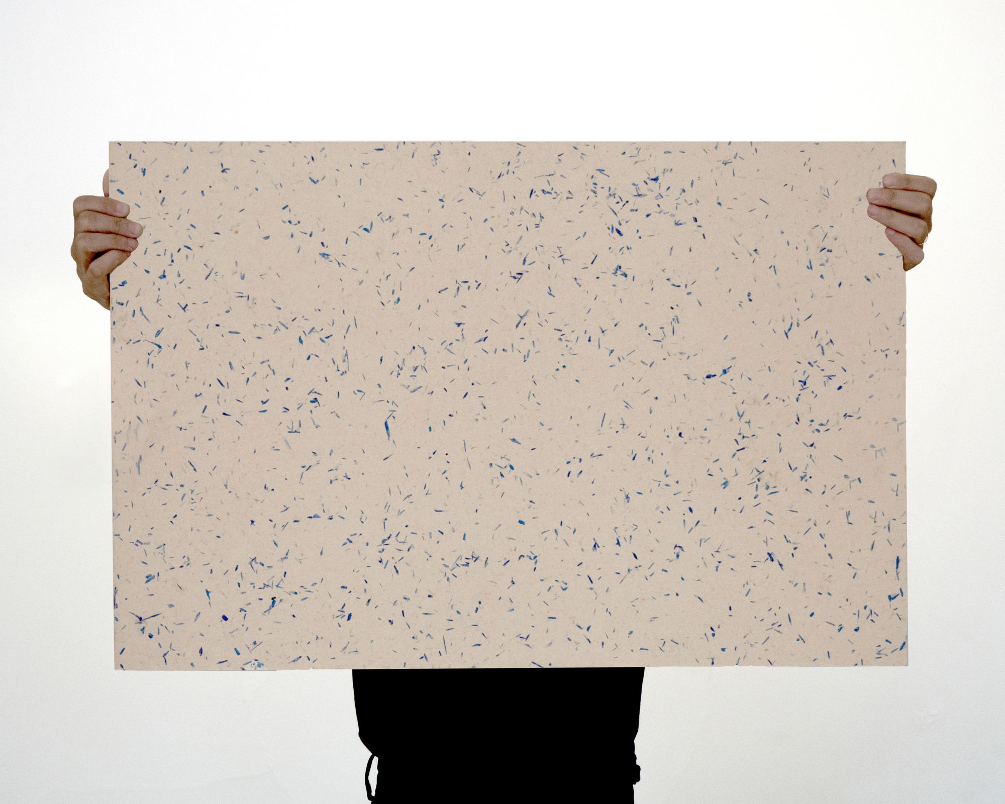 The product designer holds a rectangular sample board with both hands stretched out in front of her in such a way that only her hands and part of her torso are visible. The board is cream in color and speckled with dark blue spots (similar to terrazzo).