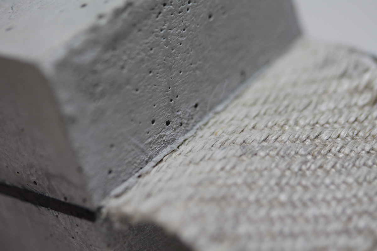 The photo shows a textile fabric with a coarse weave structure embedded between two layers of very fine-grained concrete.