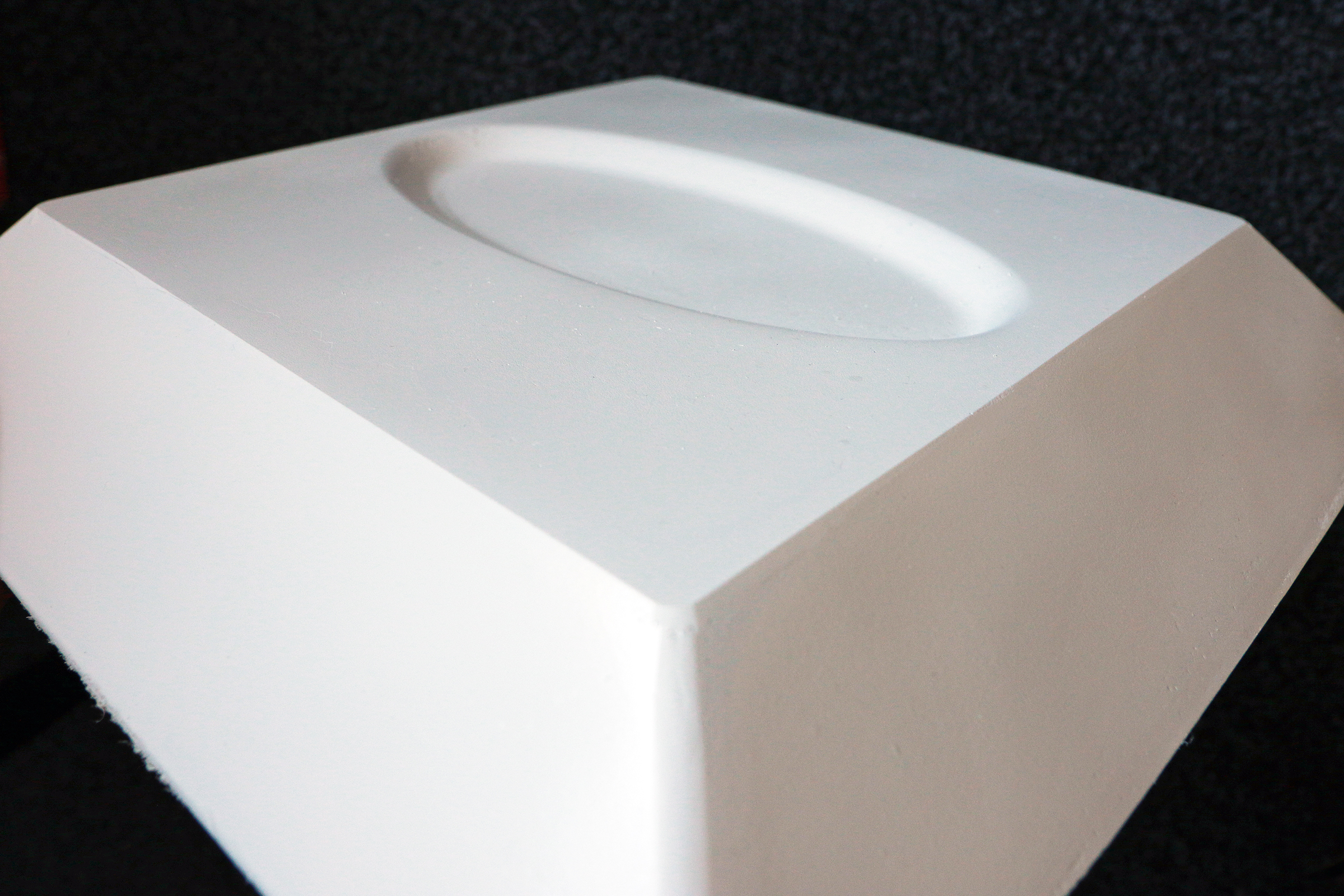 The photo shows a white component in the shape of a pyramid without a tip. There is an oval indentation on the top.