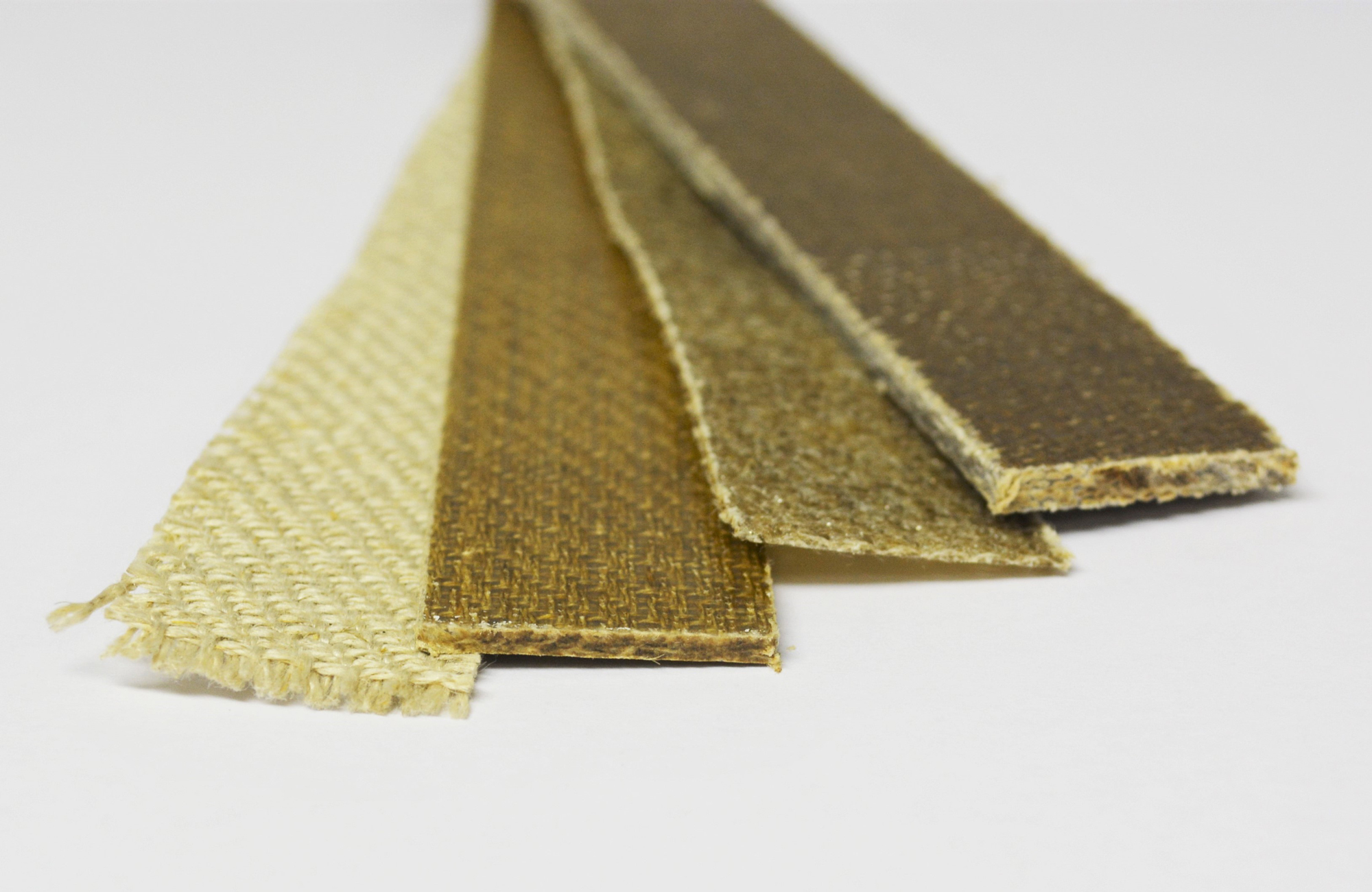 Flax-NFK test specimen Vier Streifen Flachsgewebe in unterschiedlicher Dicke und Farbintensität liegen auf einer Tischplatte.