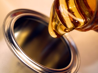 A viscous, honey-colored liquid is poured from a glass vessel into a metal container.