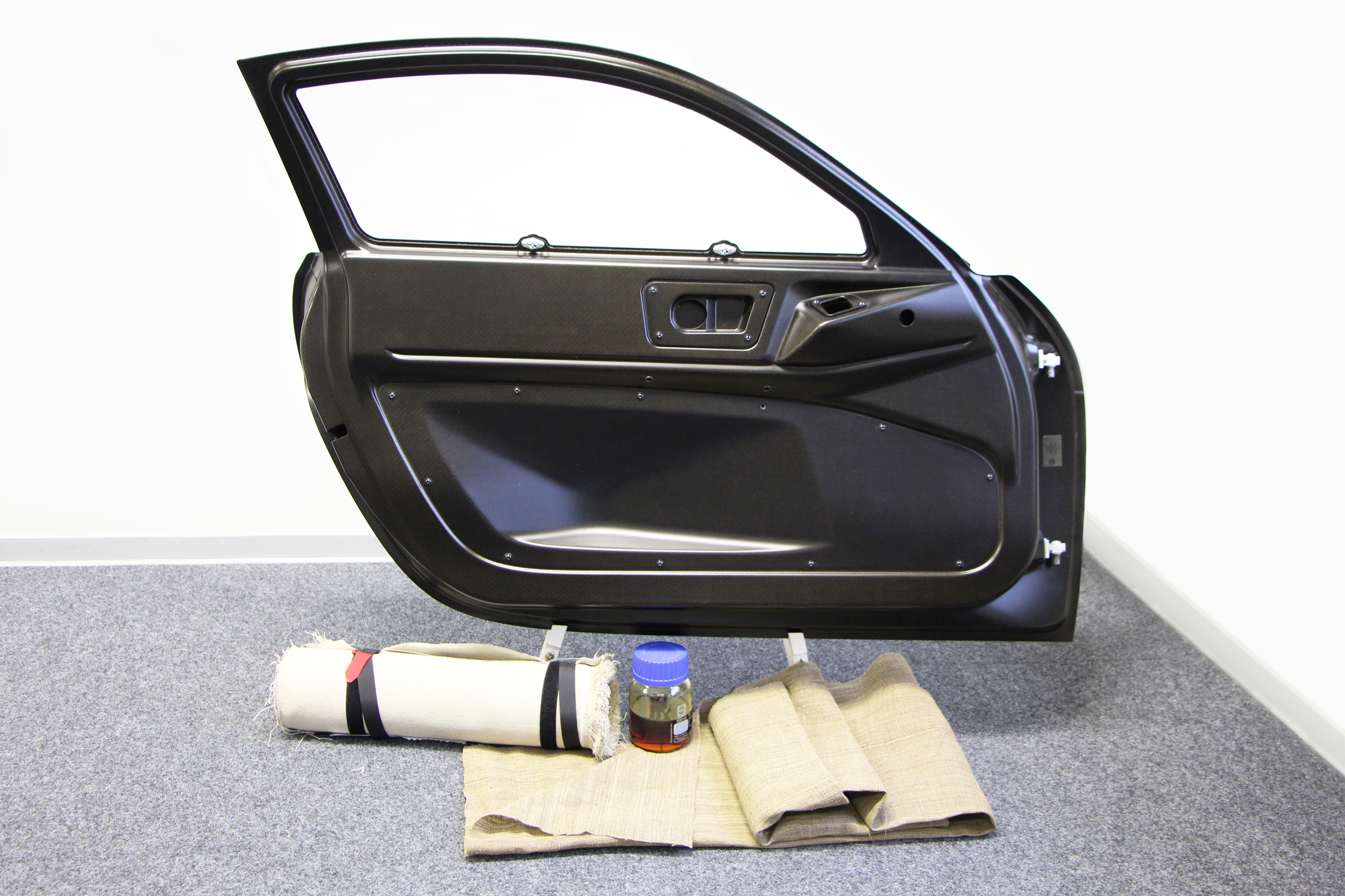 A car door is positioned behind mats made from flax and a glass jar containing resin. 