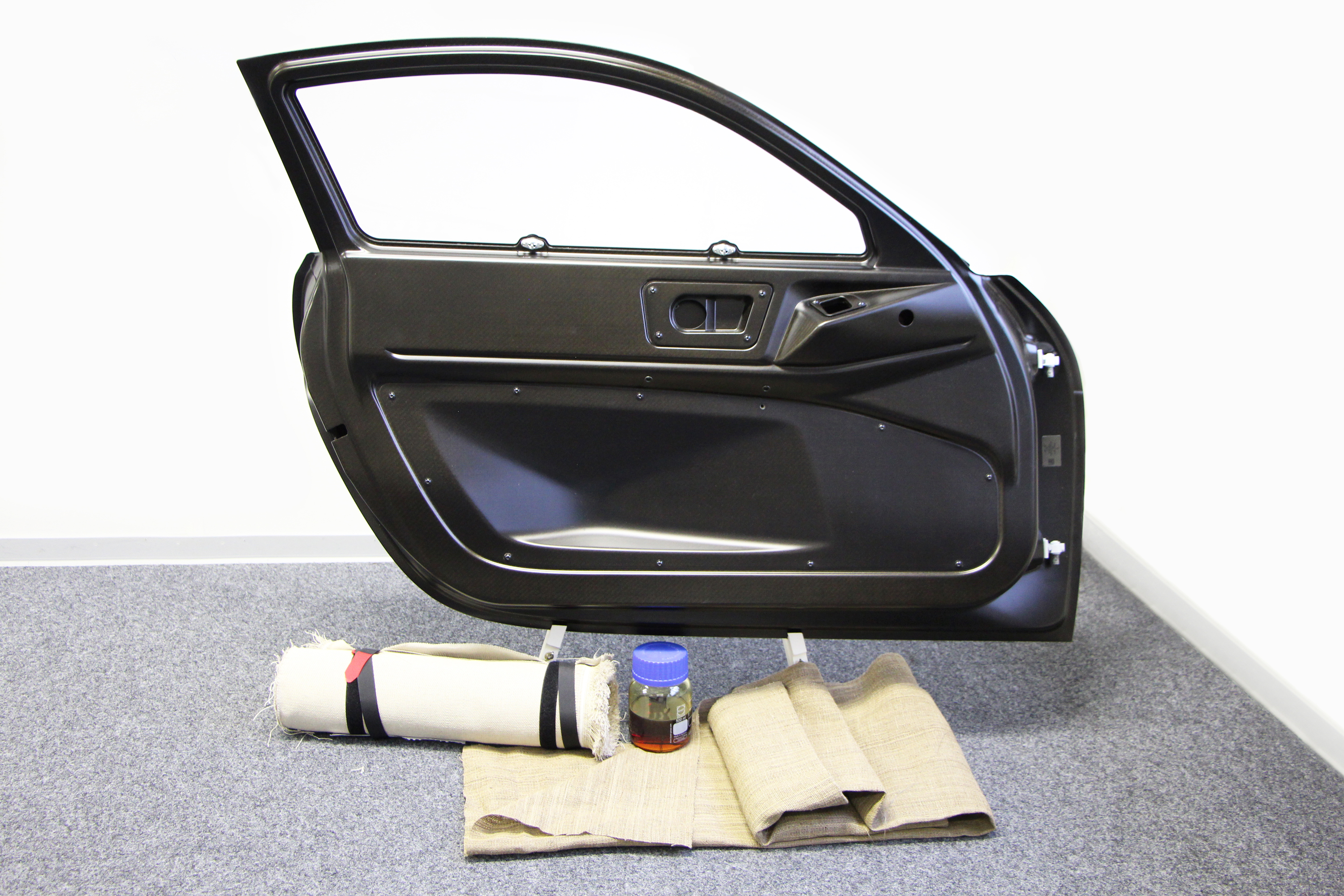 Bio-based vehicle door A car door is positioned behind mats made from flax and a glass jar containing resin.