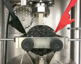 The photo shows an asphalt test specimen with integrated sensor fabric in a testing machine.
