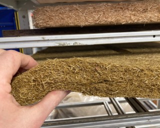 Flexible insulation mats made from wheat straw The photo shows a hand which is holding and slightly bending an approximately 5 cm thick flexible insulation mat made from wheat straw.