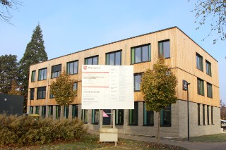 The photo shows a three-story modern office building with a facade of clinker and wood.