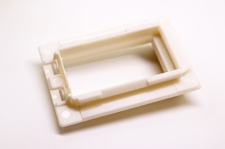 The photo shows an approximately palm-sized, frame-like object made from white bioplastic that is used for the insulated feed-through of cables and busbars.