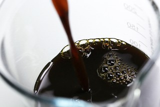 The image shows a measuring cup into which a brown-colored liquid is being poured. 