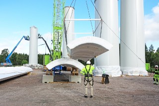 The photo shows a construction site, with a construction worker in the centre and a quarter shell being moved by a crane.