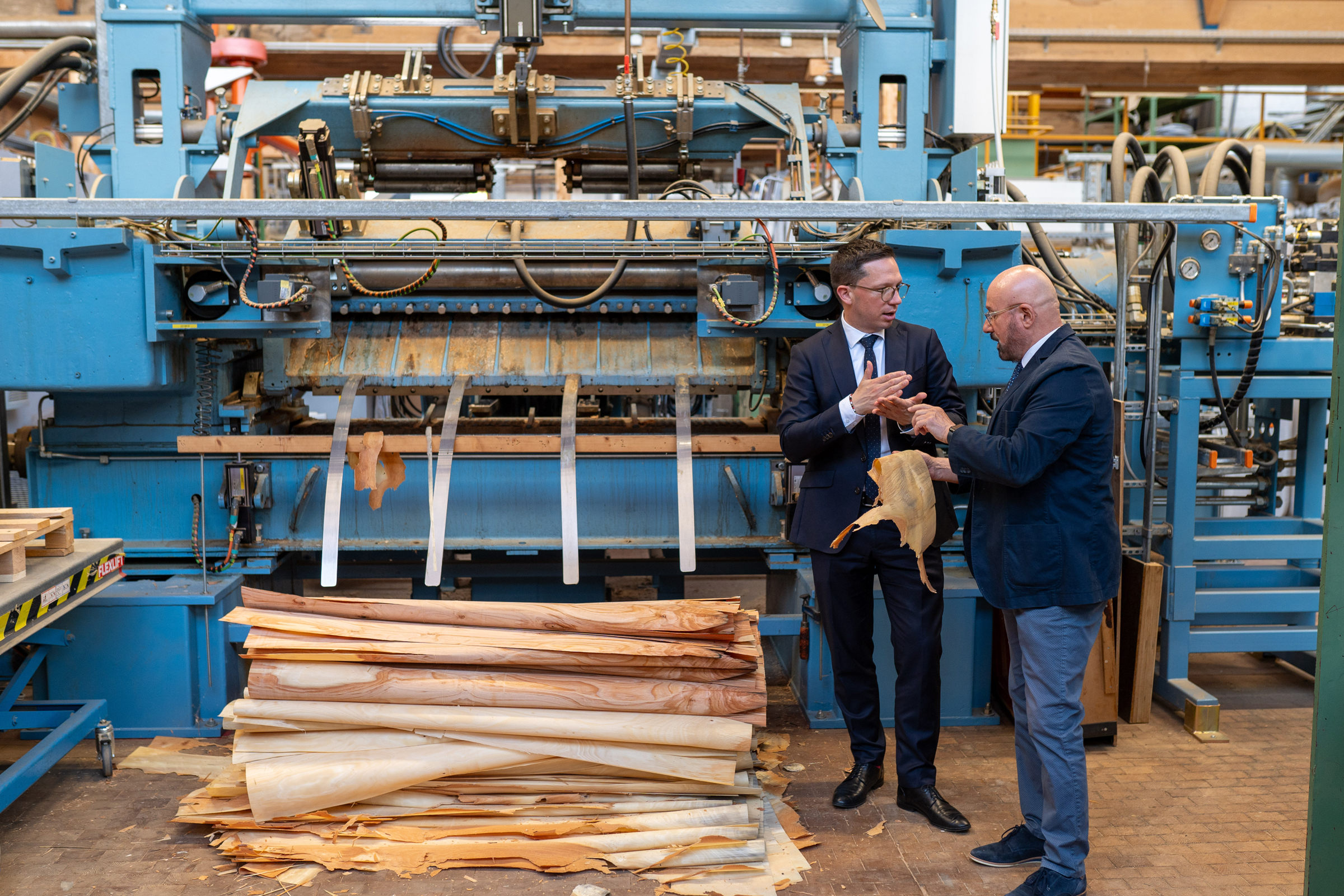 Science Minister Falko Mohrs visits the Fraunhofer WKI The photo shows Minister Falko Mohrs and Institute Director Professor Kasal in front of a large technical plant on which wood veneer is being produced.