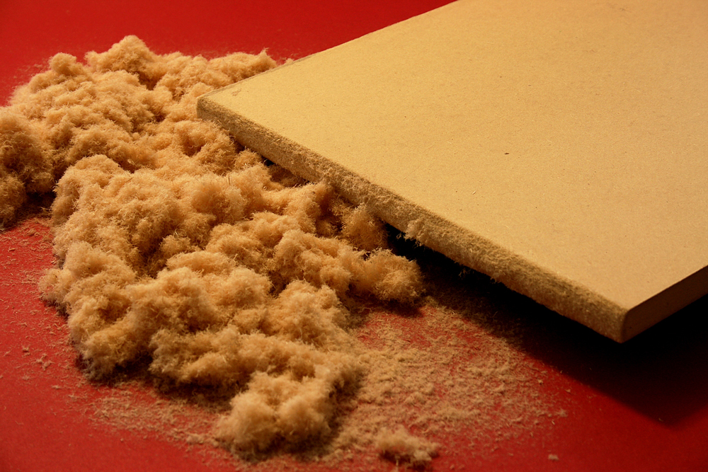 Stück einer MDF-Platte mit sichtbarer Sägekante liegt neben einem Haufen Holzfasern.
