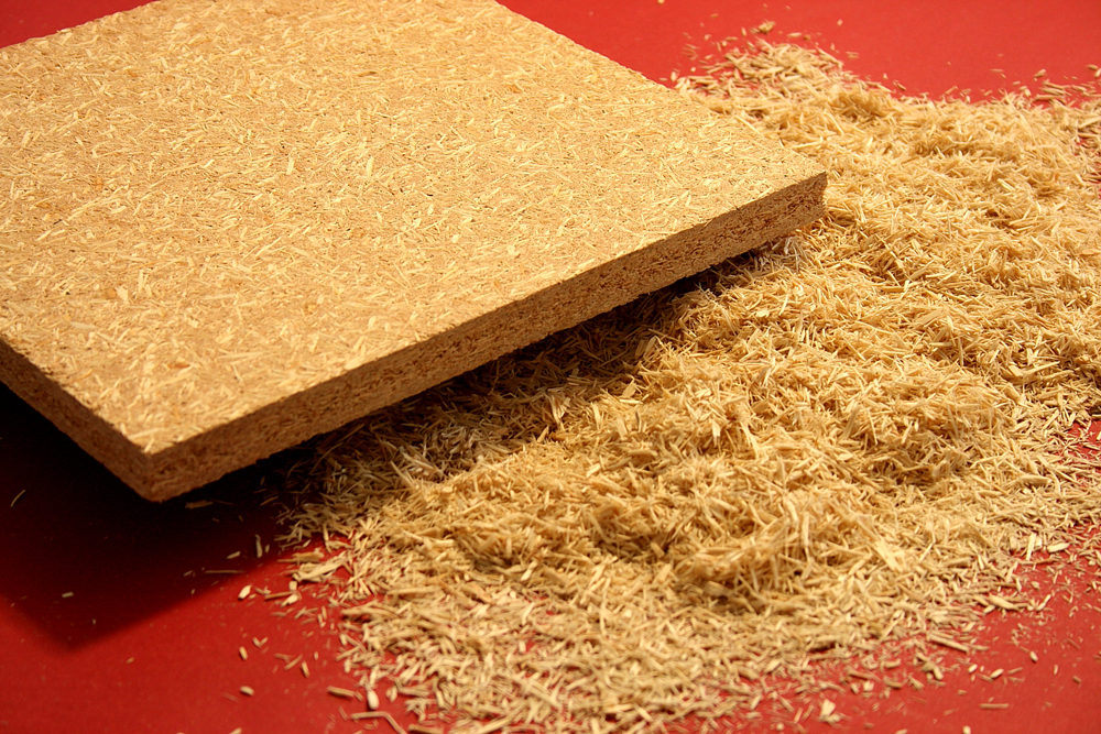 Stück einer Spanplatte mit sichtbarer Sägekante liegt neben einem Haufen Holzspänen.