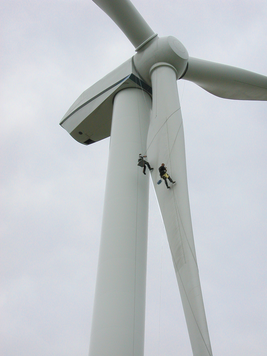 Two people abseil down the blade of a wind turbine.