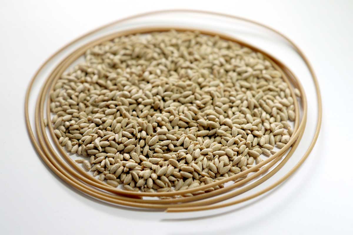 The photo shows a small pile of cereal-grain-shaped, brownish granules and a cable-shaped piece of filament in the same color.