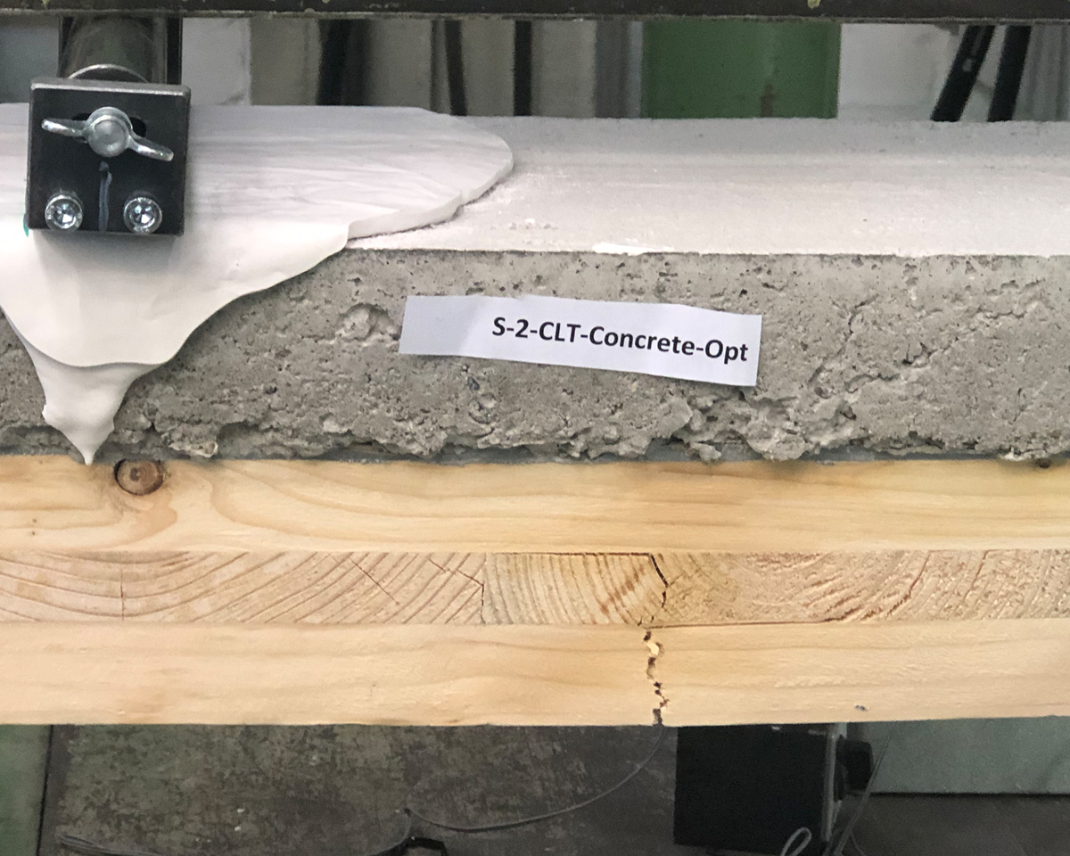 The close-up shows a building component consisting of three layers (from bottom to top): cross-laminated timber (80 mm), thin adhesive layer, concrete (50 mm). The cross-laminated timber has a crack that extends from the bottom of the beam to the top.