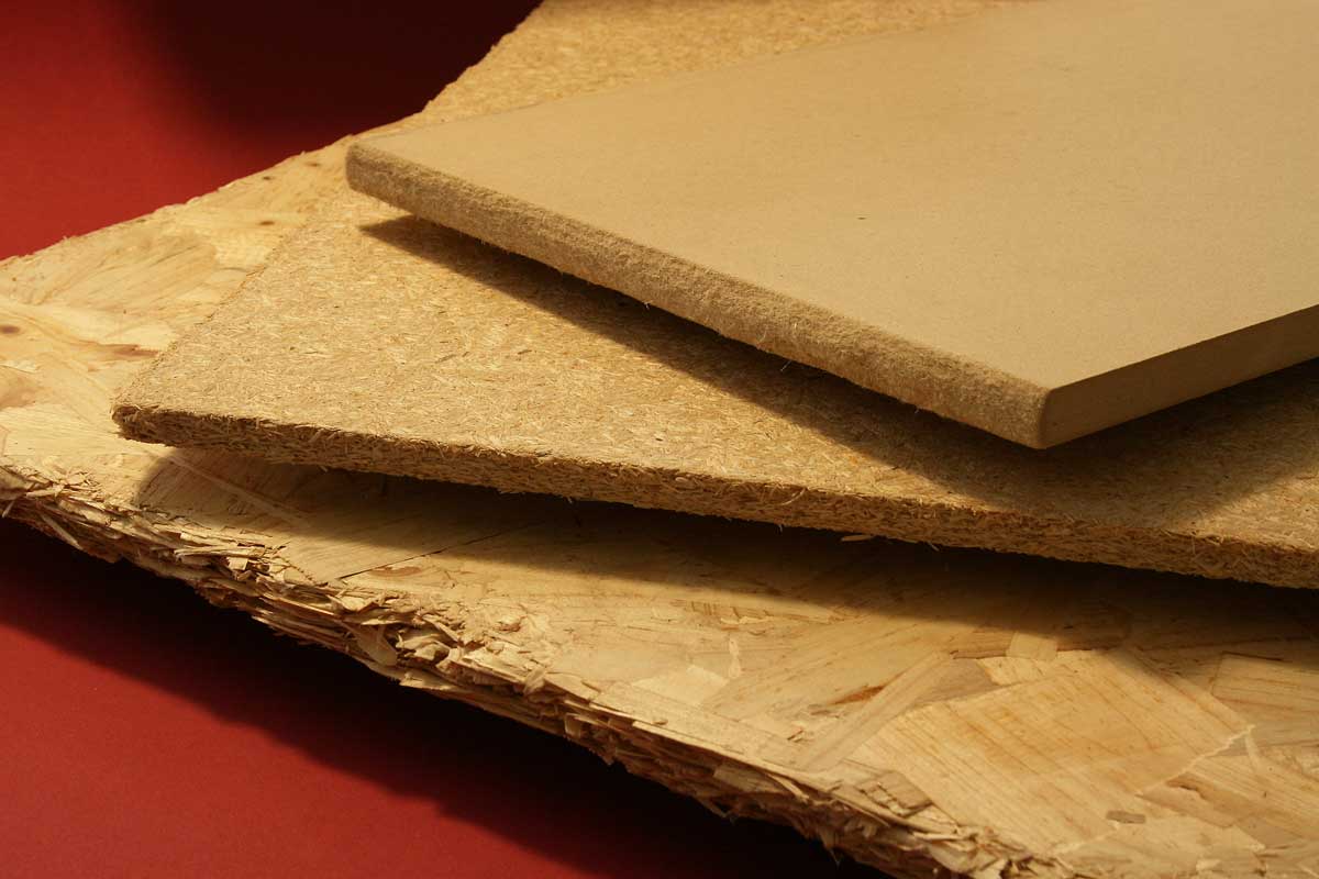 The photo shows sample pieces of three different wood-based materials (OSB, particle board and MDF).