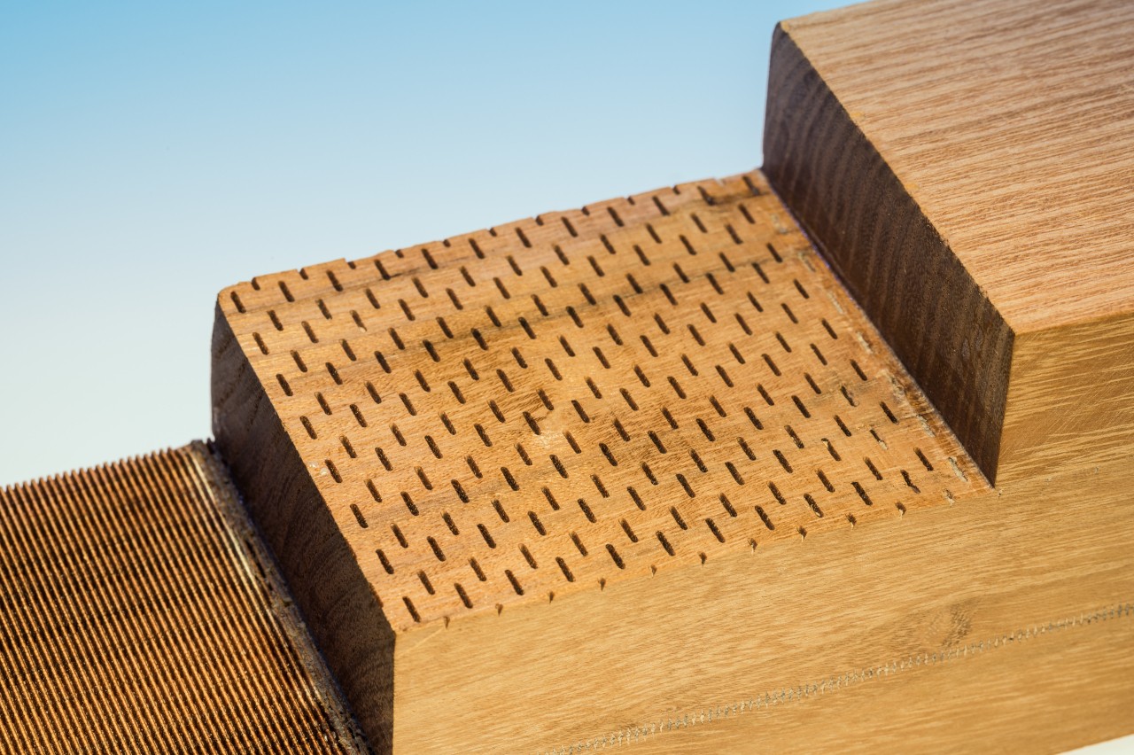 The photo shows individual layers of a glued laminated timber with a surface structure that looks similar to perforated sheeting.
