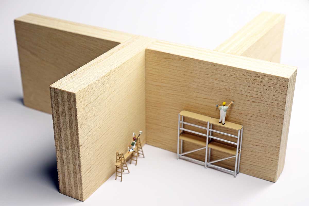The photo shows a model of a room layout with plywood panels and miniature figures.