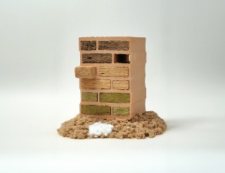 The photo shows a commercially available, vertically positioned masonry brick with 12 evenly spaced cavities. The cavities are filled with a variety of fiber-mat types. In front of the brick is a large pile of brown beech-wood fibers and a small pile of white bico fibers.