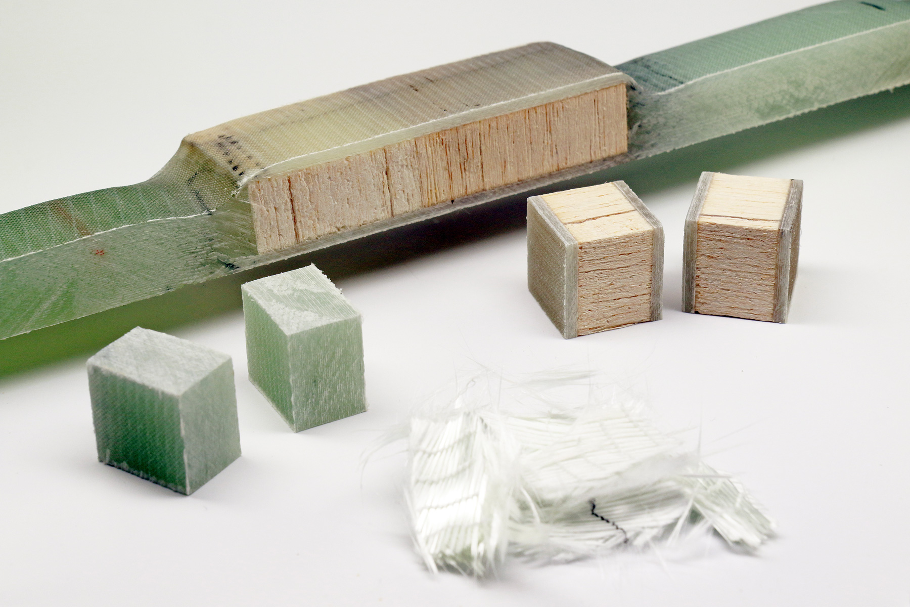 Wind power rotor blades: material samples (balsa wood, GRP) The photo shows, lying next to one another: a small piece of white glass-fiber fabric, and balsa-wood blocks that are embedded in a greenish plastic layer.