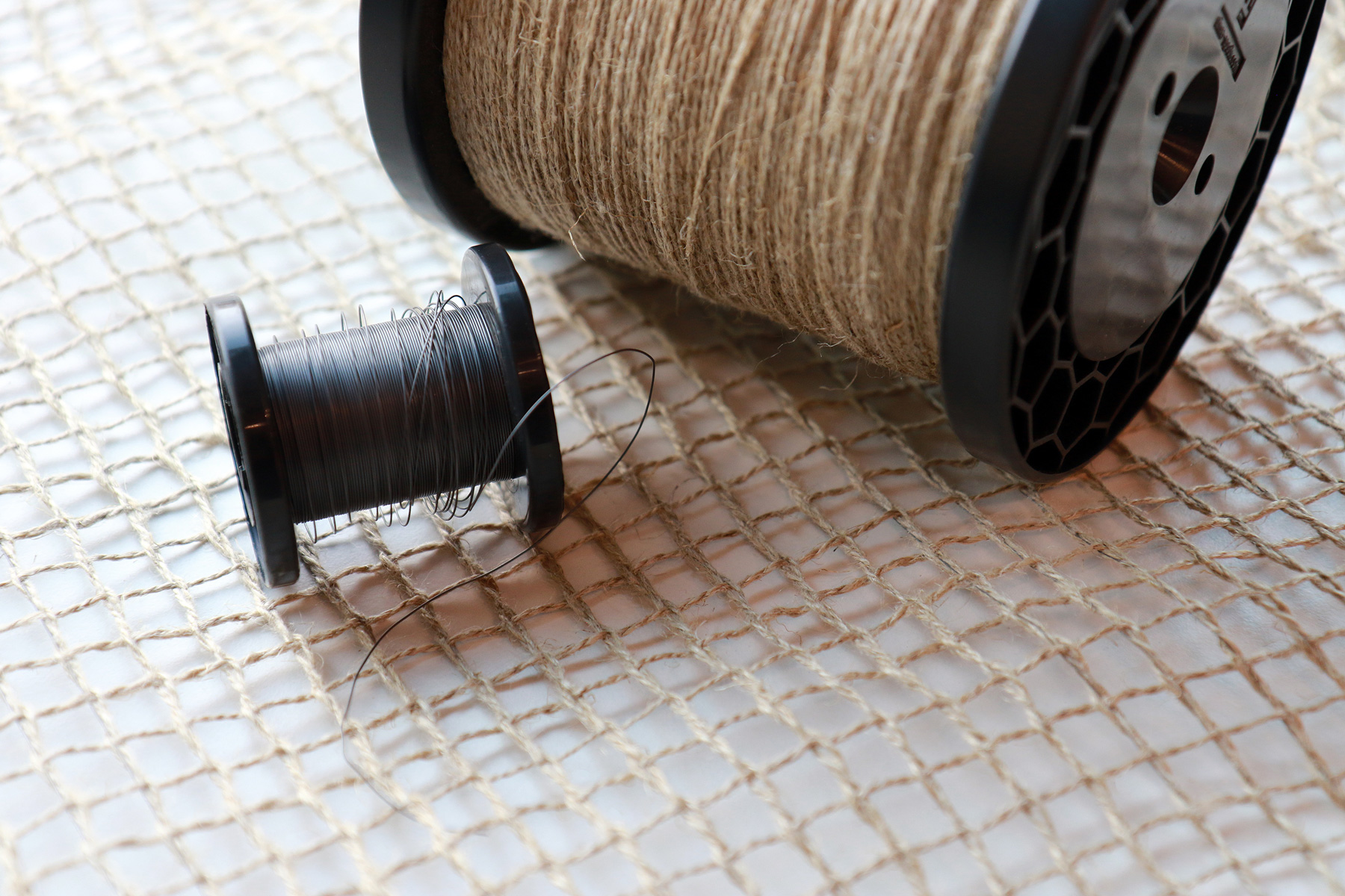 The photo shows a net-like fabric upon which two spools of yarn lie: a large spool with flax-fiber yarn, and a small spool with wire