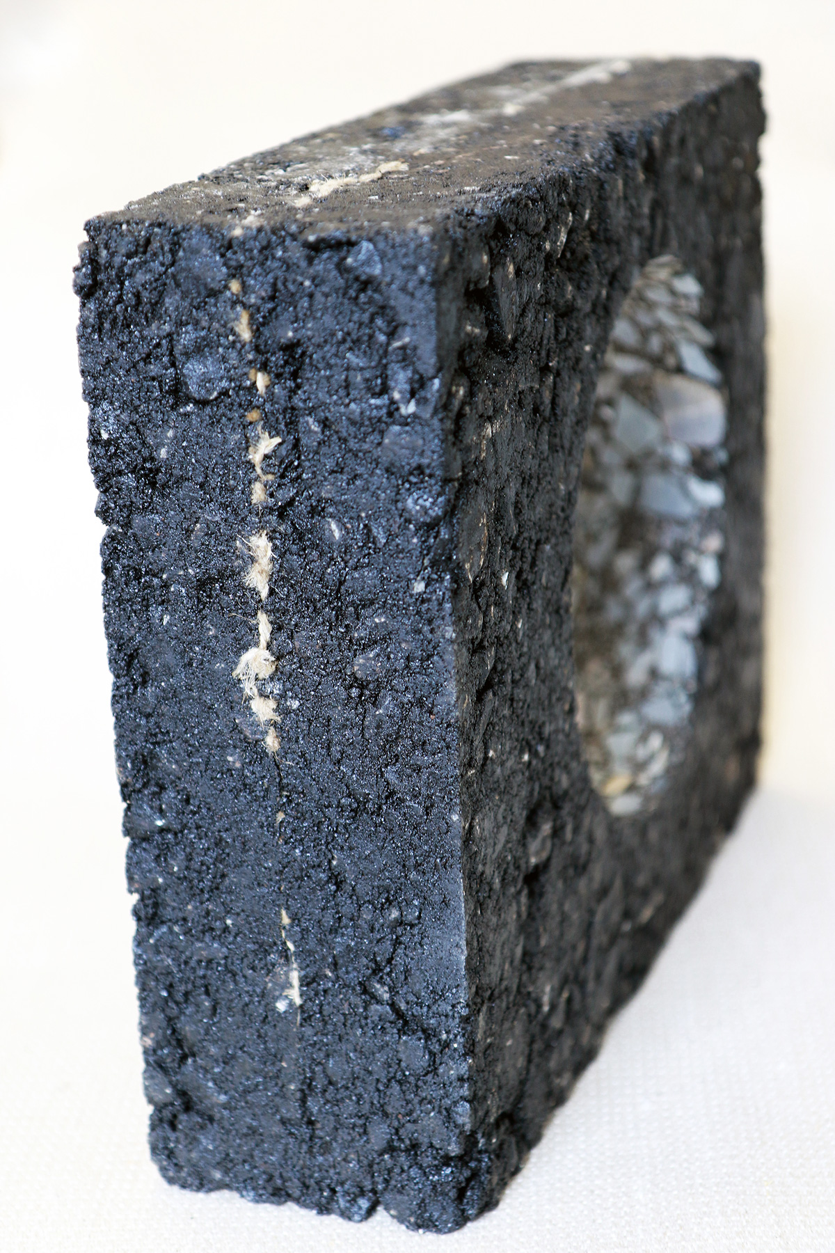 The photo shows an asphalt block the size of a briefcase, with a core hole of around 15 cm in diameter. The sensor fabric embedded in the asphalt block is clearly visible on the outer walls of the block, but almost invisible on the very smooth inner wall of the core hole.
