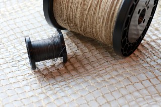 The photo shows a net-like fabric upon which two spools of yarn lie: a large spool with flax-fiber yarn, and a small spool with wire
