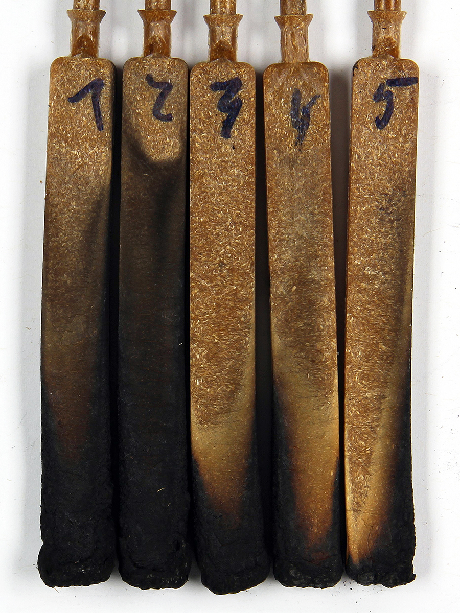 The photo shows five WPC test rods with black discoloration (burn marks) of varying intensity.